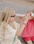 Two kids play outside, peering through mushie Kaleidoscopes.