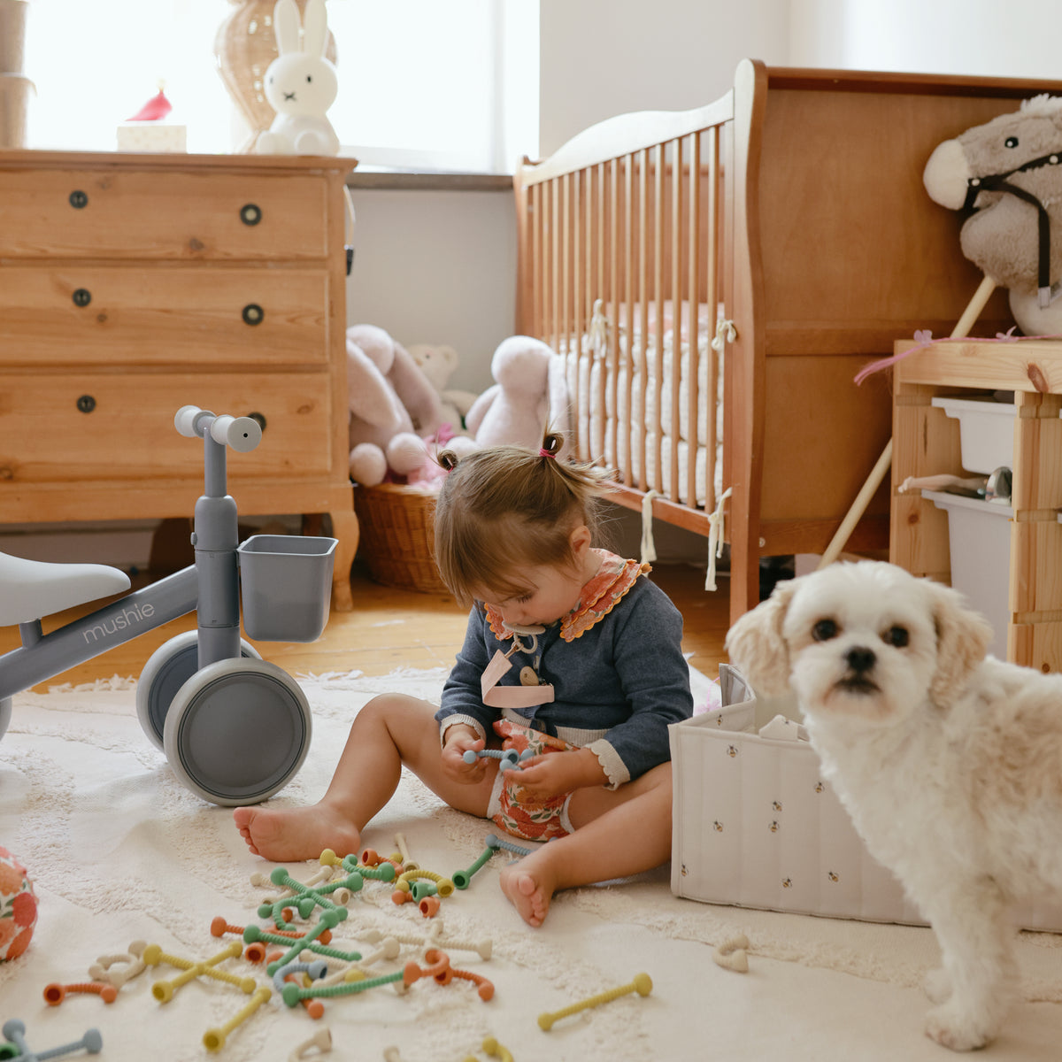 A mushie Diaper Caddy sits in the nursery as a toddler plays near a small white dog.