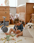 A mushie Diaper Caddy sits in the nursery as a toddler plays near a small white dog.
