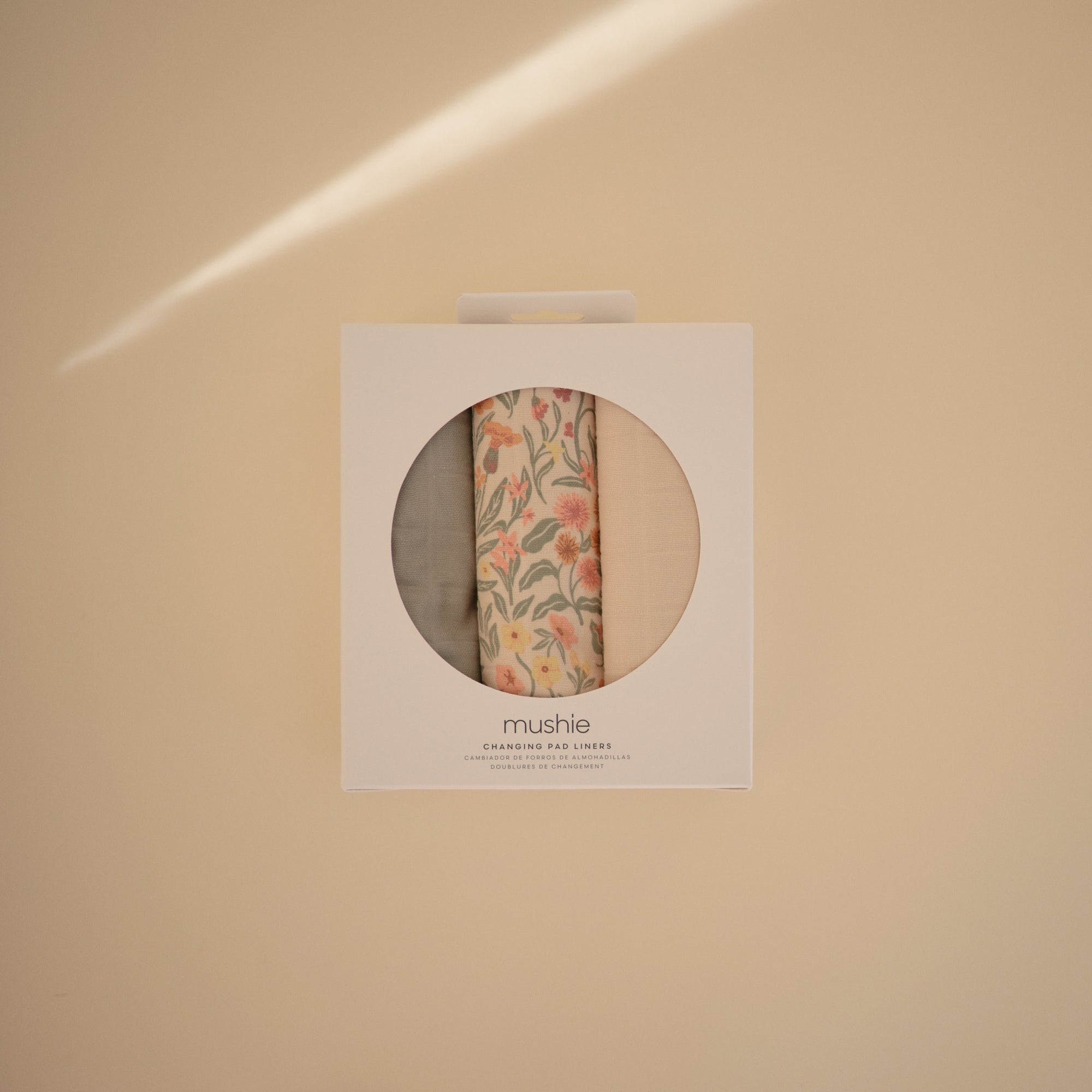 Mushie Changing Pad Liners: set of 3 muslin, one floral, shown on a beige background.