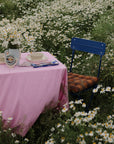 Table with mushie Round Dinnerware Bowl, pink cloth, and flowers in a field by a blue chair.