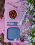A picnic with strawberries, flowers, and a mushie Round Dinnerware Bowl on a pink cloth.