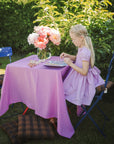 A girl uses the mushie Reusable Sticker Set at a purple table outdoors.