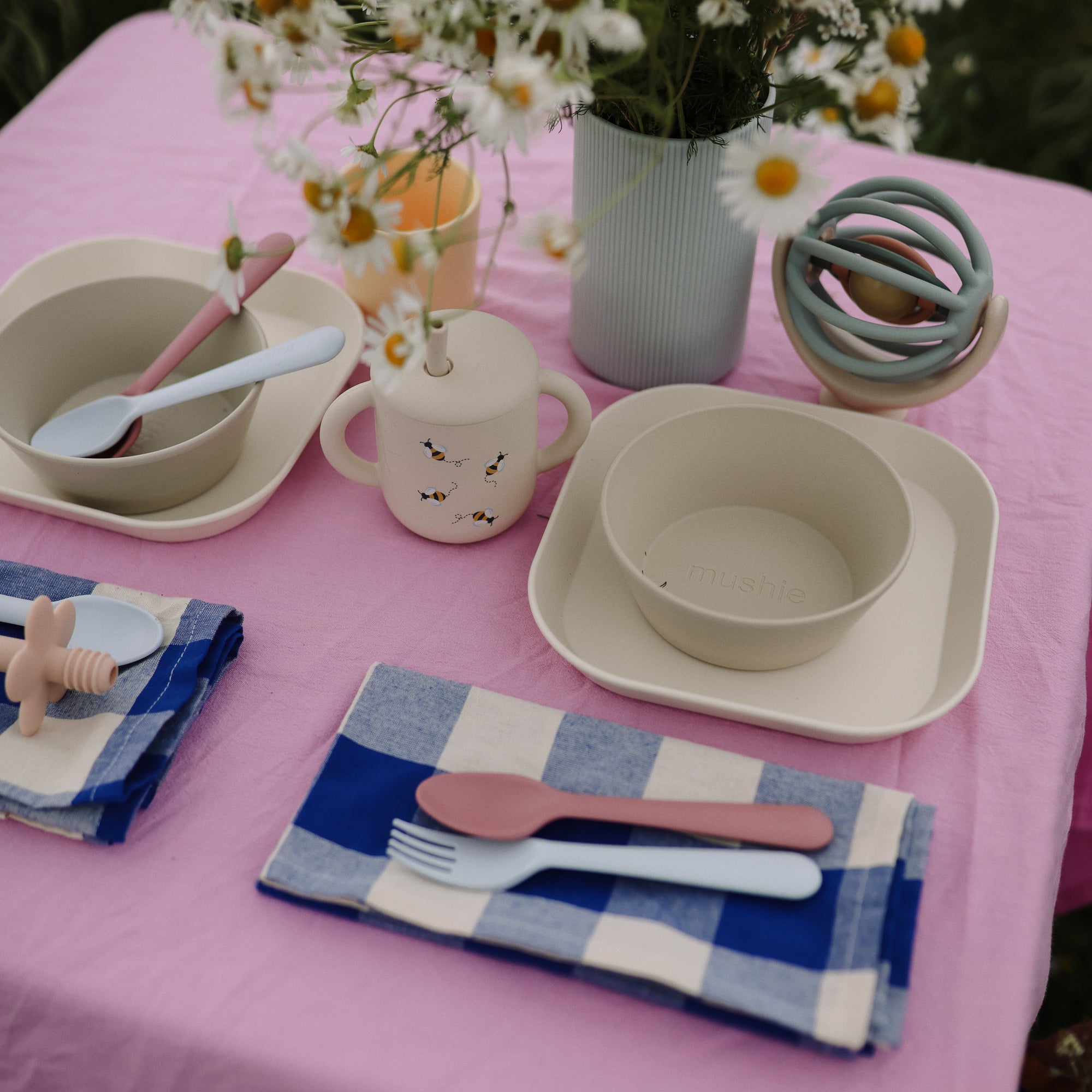 Mushie Silicone Training Cup + Straw featured in a children’s table setting with bowls and utensils.