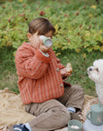 A child sits on a blanket using a mushie Kaleidoscopes next to a small white dog.