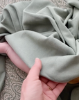 A behind the scenes sneak peek of the mushie team designing the blanket in a white room, comparing swatches of cloth, then transitioning to seeing the full ribbed baby blanket with a little baby. 