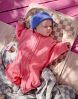 Baby in pink onesie and blue hat on Mushie Changing Pad Liners, with a checkered blanket.