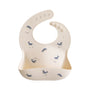 The mushie Silicone Baby Bib in Whales features a cream color with blue whale designs, a wide pocket, and adjustable neck strap. Easy to clean, it ensures stress-free mealtimes for your baby.