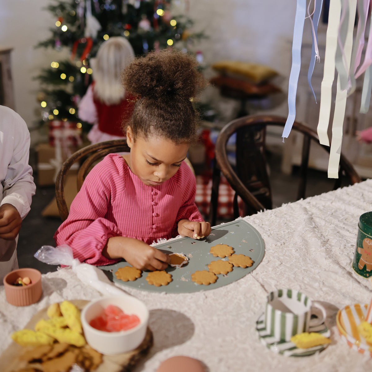 A girl packs snacks in mushie Silicone Baby Food Containers at a festive cookie decorating table.